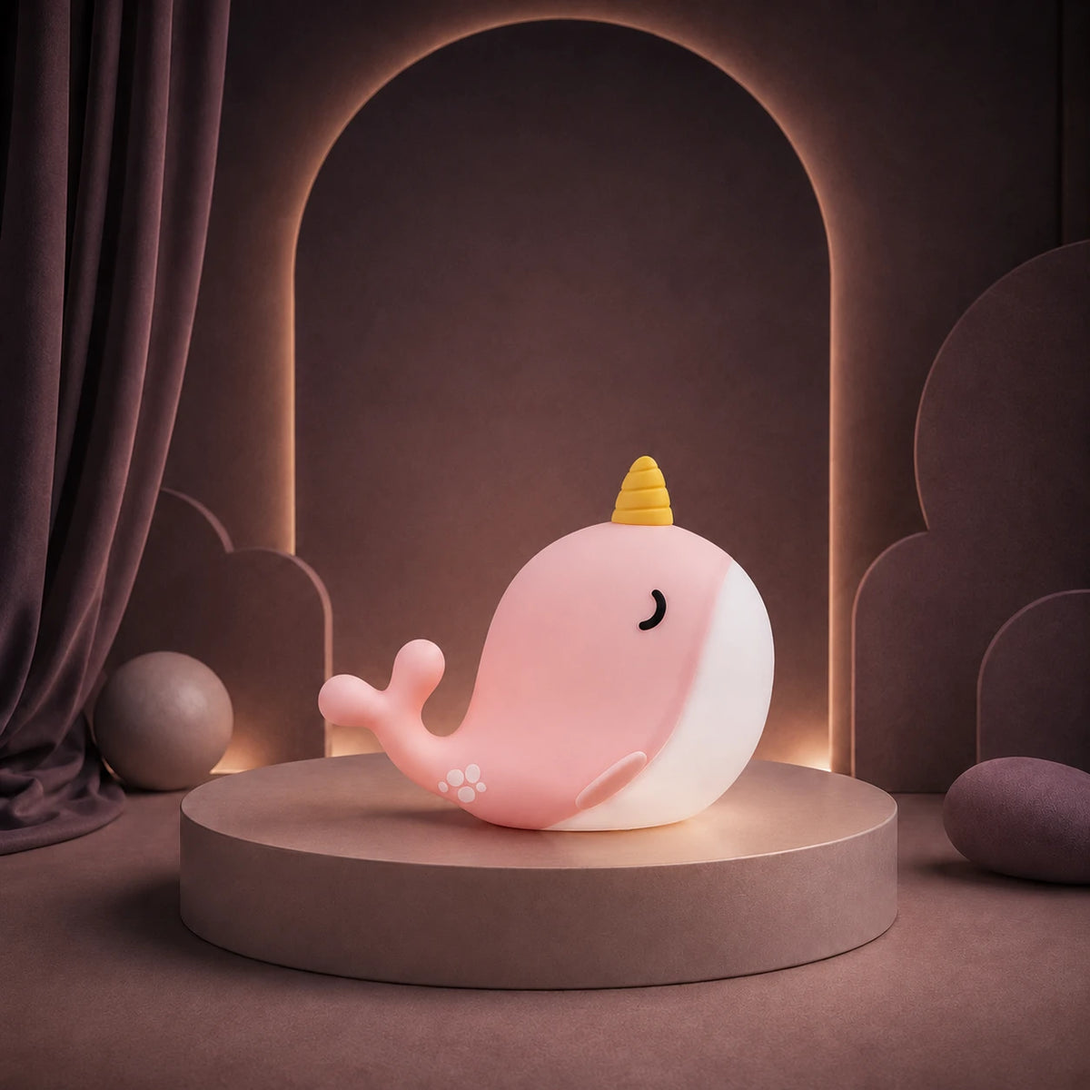Veilleuse en forme de baleine narval rose allumée sur un podium mauve.