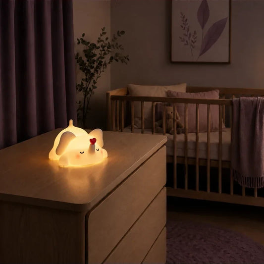 Veilleuse en forme d’éléphant endormi avec un cœur rouge allumée sur une commode dans une chambre de bébé.