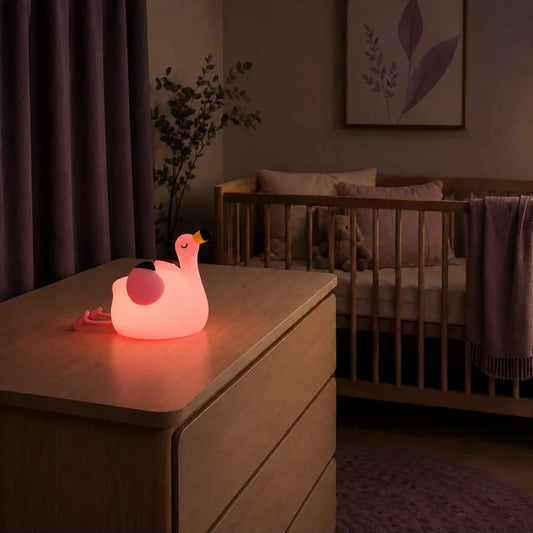 Veilleuse en forme de flamant rose allumée sur une commode dans une chambre de bébé.