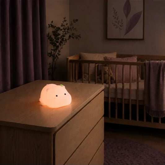 Veilleuse rose en forme d’hippopotame rond allumée sur une commode dans une chambre de bébé.