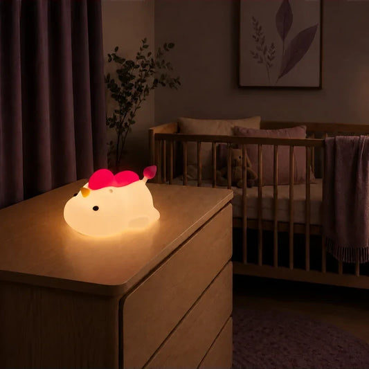 Veilleuse en forme de licorne allongée à crinière rose allumée sur une commode dans une chambre de bébé.