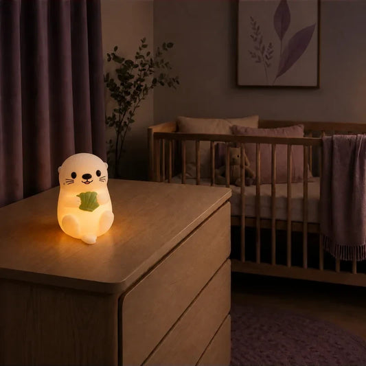 Veilleuse en forme de loutre tenant une feuille verte allumée sur une commode dans une chambre de bébé.