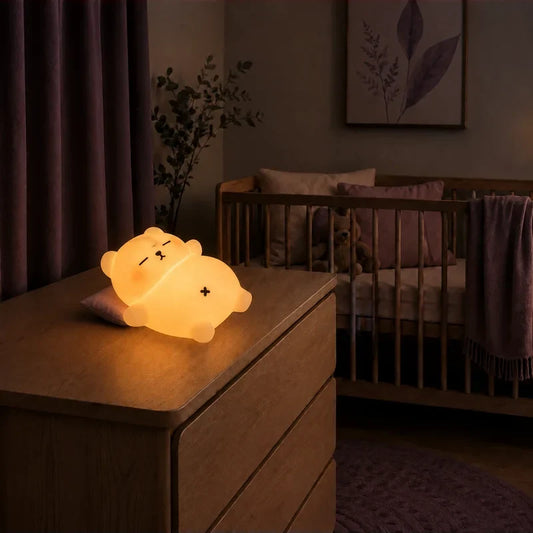 Veilleuse en forme d’ours allongé sur le dos allumée sur une commode dans une chambre de bébé.