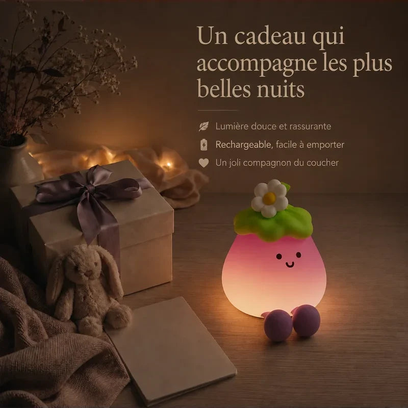 Veilleuse en forme d’aubergine souriante présentée dans une ambiance cadeau avec une boîte et un ruban.