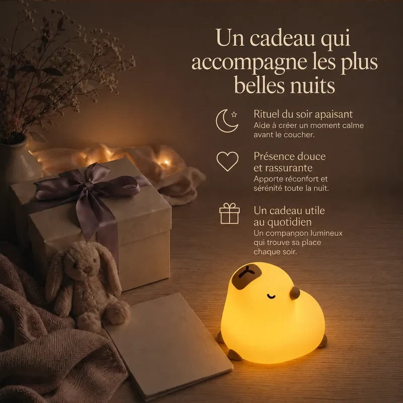 Veilleuse en forme de capybara rond présentée dans une ambiance cadeau avec une boîte et un ruban.