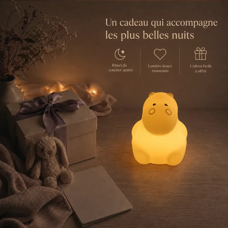 Veilleuse en forme d’hippopotame assis présentée dans une ambiance cadeau avec une boîte et un ruban.