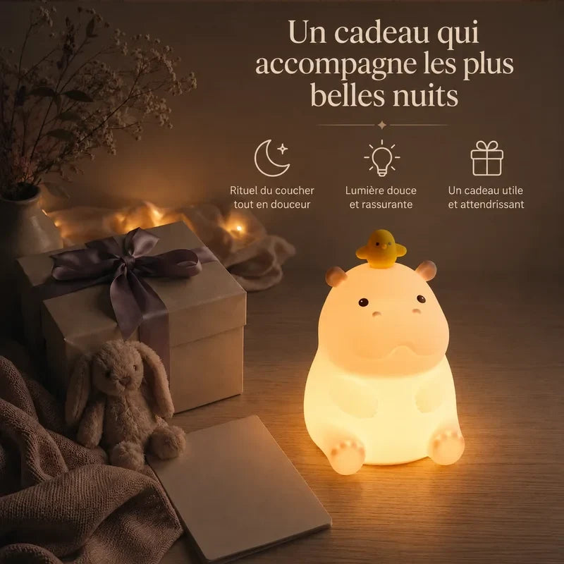 Veilleuse en forme d’hippopotame avec un caneton sur la tête présentée dans une ambiance cadeau avec une boîte et un ruban.