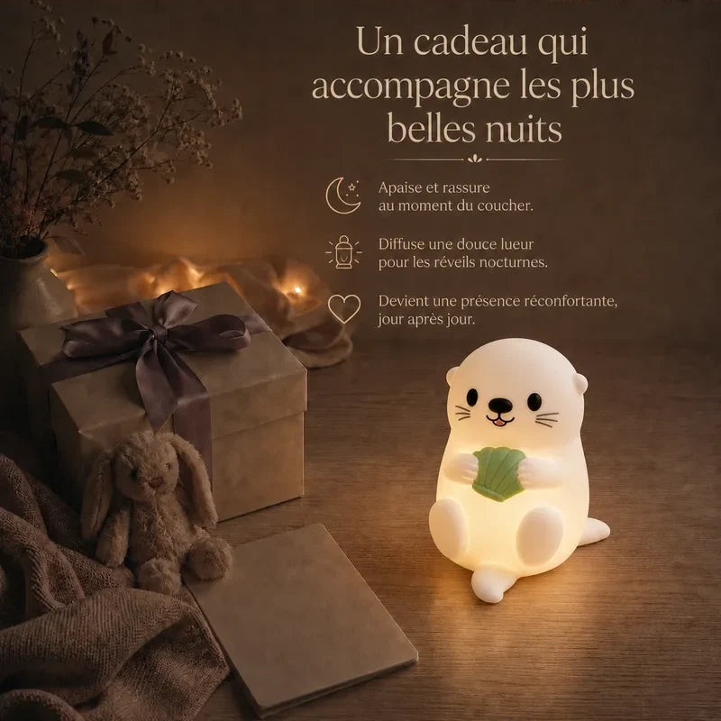Veilleuse en forme de loutre tenant une feuille verte présentée dans une ambiance cadeau avec une boîte et un ruban.