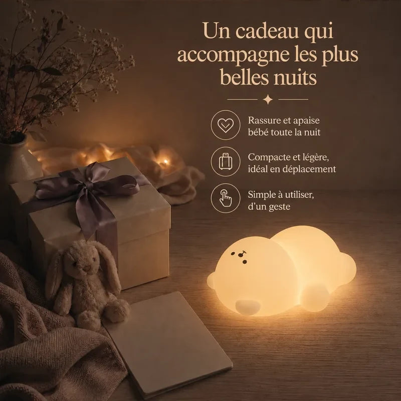 Veilleuse en forme d’ours endormi allongé présentée dans une ambiance cadeau avec une boîte et un ruban.