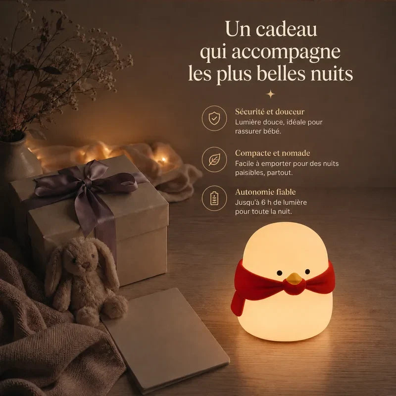 Veilleuse en forme de pingouin avec une écharpe rouge présentée dans une ambiance cadeau avec une boîte et un ruban.