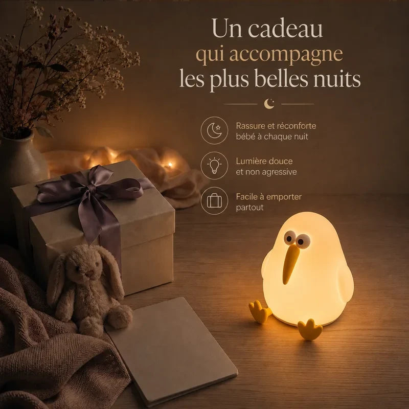 Veilleuse en forme de pingouin à long bec présentée dans une ambiance cadeau avec une boîte et un ruban.