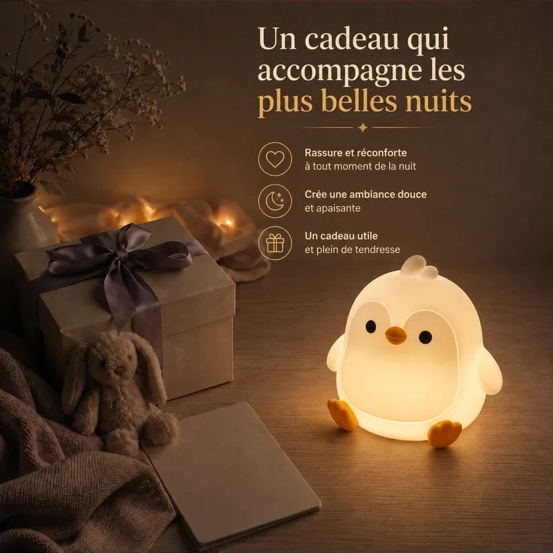 Veilleuse en forme de pingouin rond présentée dans une ambiance cadeau avec une boîte et un ruban.