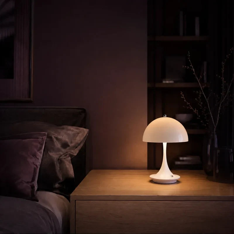 Lampe champignon blanc allumée sur une table de chevet dans une ambiance nocturne.