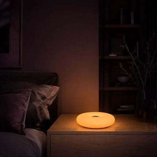 Lampe galet ovale lumineux allumée sur une table de chevet dans une ambiance nocturne.