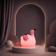 Veilleuse en forme de flamant rose allumée sur un podium mauve.