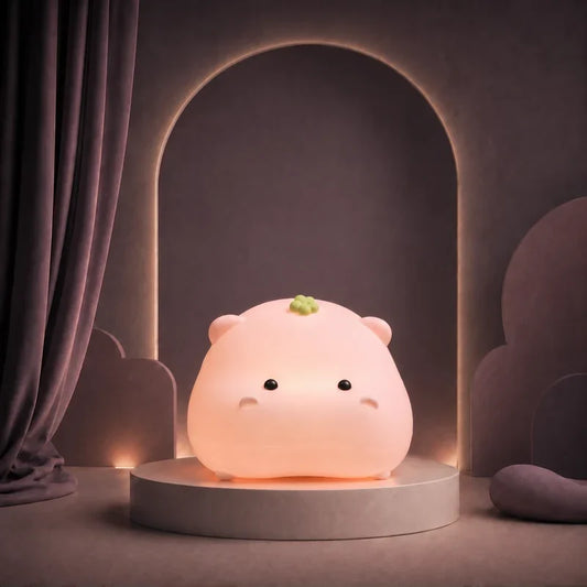 Veilleuse rose en forme d’hippopotame rond allumée sur un podium mauve.