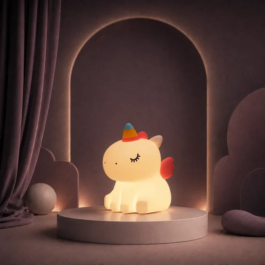 Veilleuse en forme de licorne assise à crinière multicolore allumée sur un podium mauve.