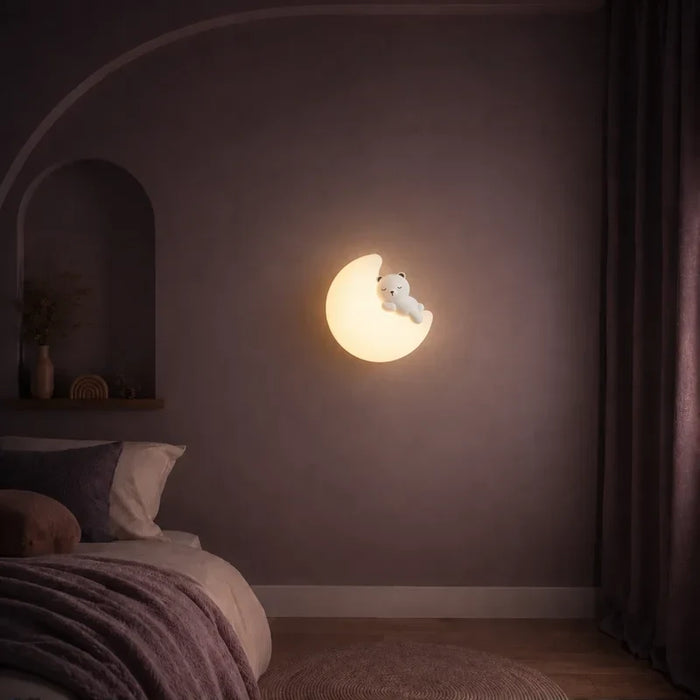 Veilleuse murale lune et ourson allumée sur un mur dans une chambre d’enfant.