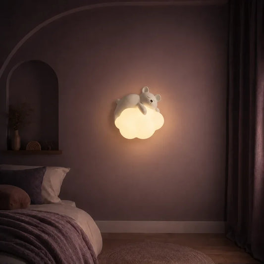 Veilleuse murale nuage avec ourson allumée sur un mur dans une chambre d’enfant.