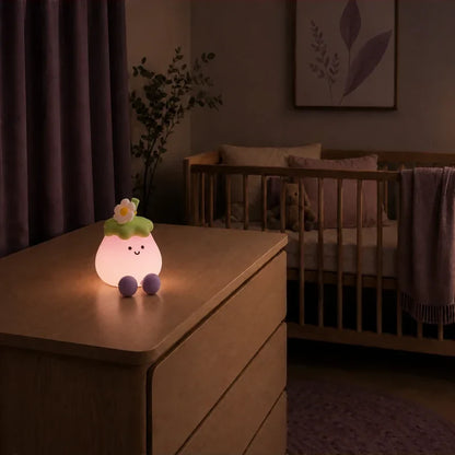 Veilleuse en forme d’aubergine souriante allumée sur une commode dans une chambre de bébé.