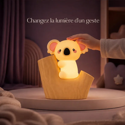 Main d’enfant touchant la veilleuse koala installée dans une souche pour changer la lumière.