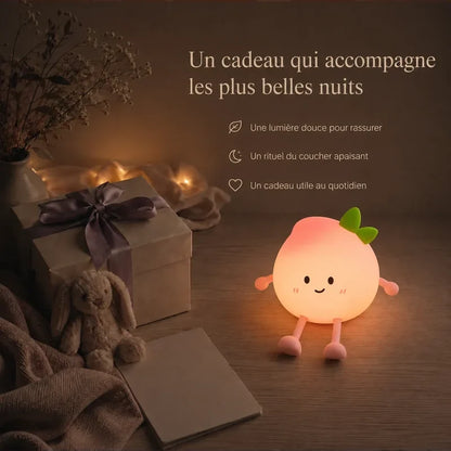 Veilleuse en forme de pêche souriante présentée dans une ambiance cadeau avec une boîte et un ruban.