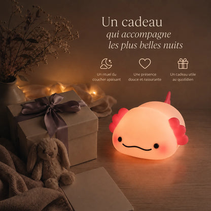 Veilleuse en forme d’axolotl allongé présentée dans une ambiance cadeau avec une boîte et un ruban.