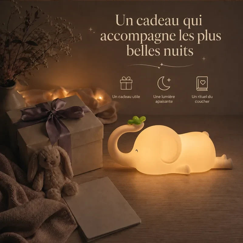 Veilleuse en forme d’éléphant allongé présentée dans une ambiance cadeau avec une boîte et un ruban.