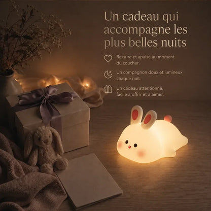 Veilleuse en forme de lapin allongé présentée dans une ambiance cadeau avec une boîte et un ruban.