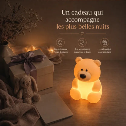 Veilleuse en forme d’ours assis présentée dans une ambiance cadeau avec une boîte et un ruban.