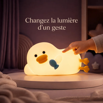 Main touchant la veilleuse en forme de canard allongé avec un petit poisson bleu pour changer la lumière.