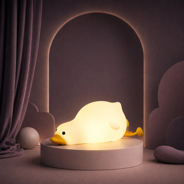 Veilleuse en forme de canard allongé allumée sur un podium mauve.